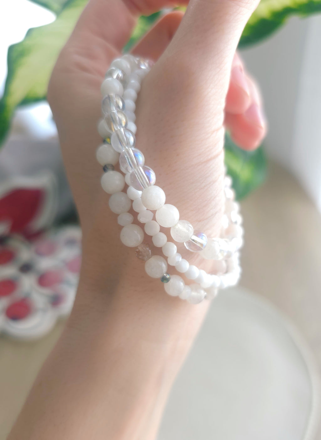 Hand showing up multiple white beaded bracelets with a blurred background
