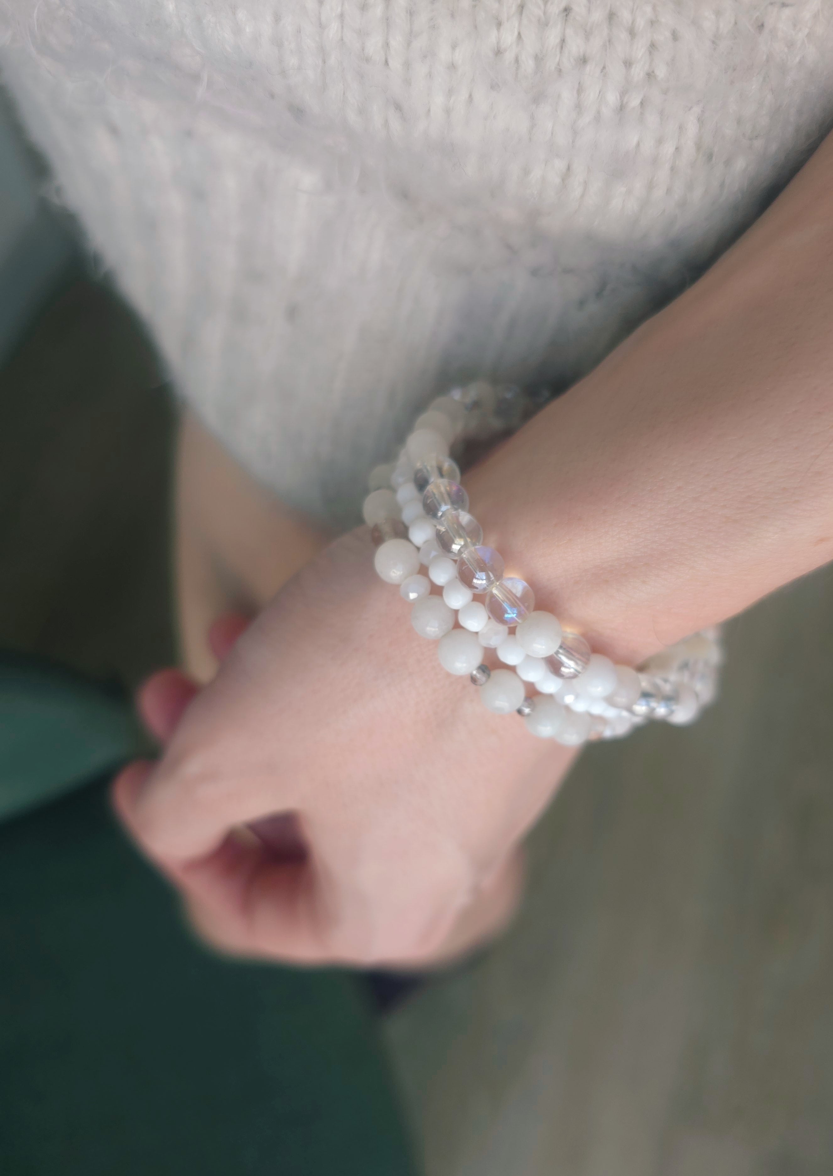 Close-up of a wrist wearing multiple beaded white bracelets with a blurred background