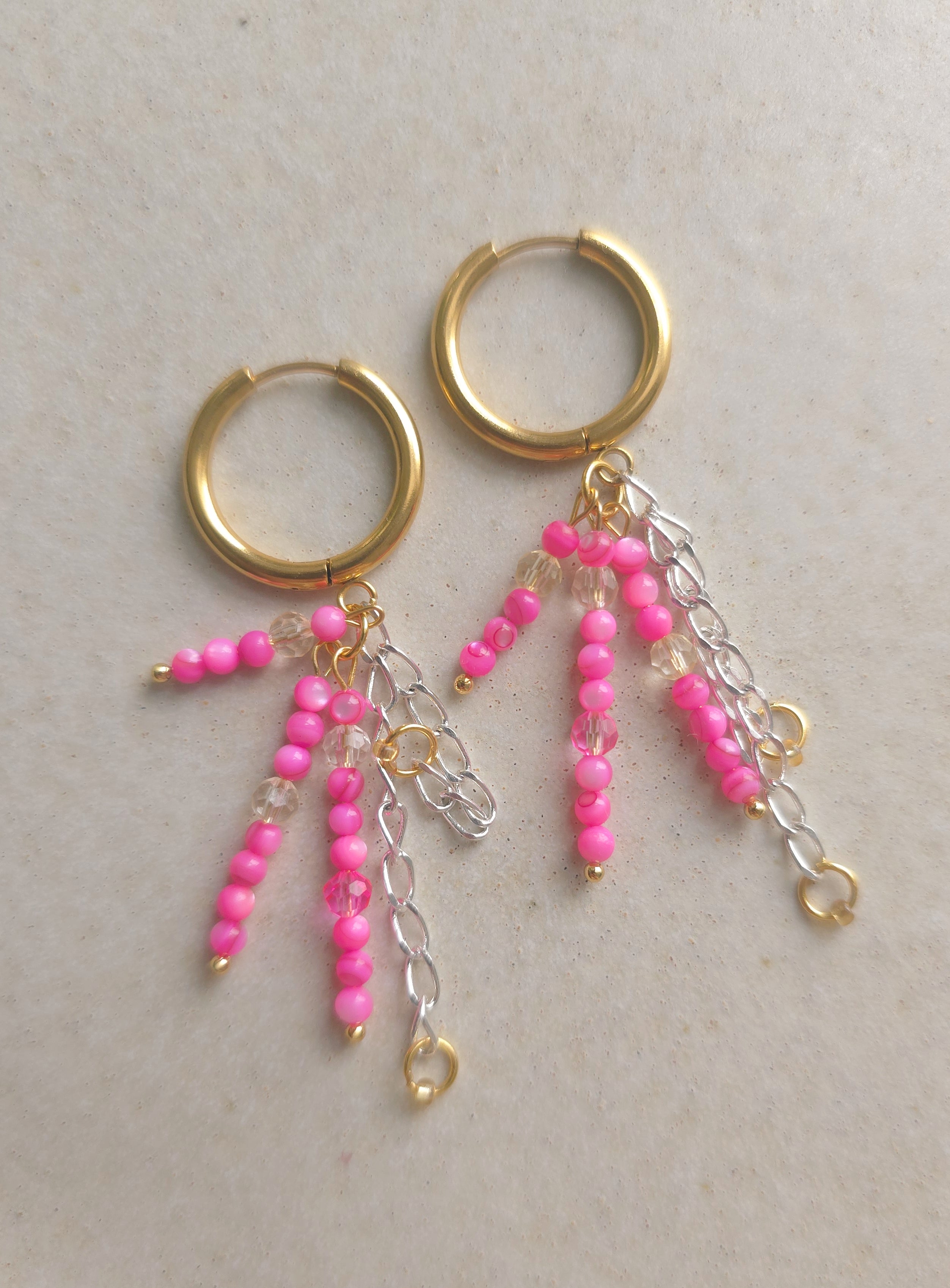 Gold hoop earrings with pink bead and chain decorations on a light background